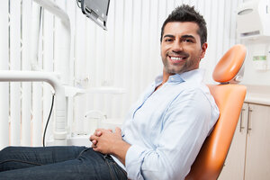 man smiling sitting in orange dentist chair, dental crowns in Topeka, KS